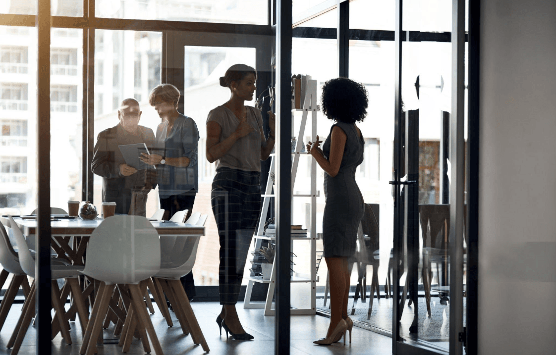 Colleagues in silhouette discussing work together in a glass-walled office