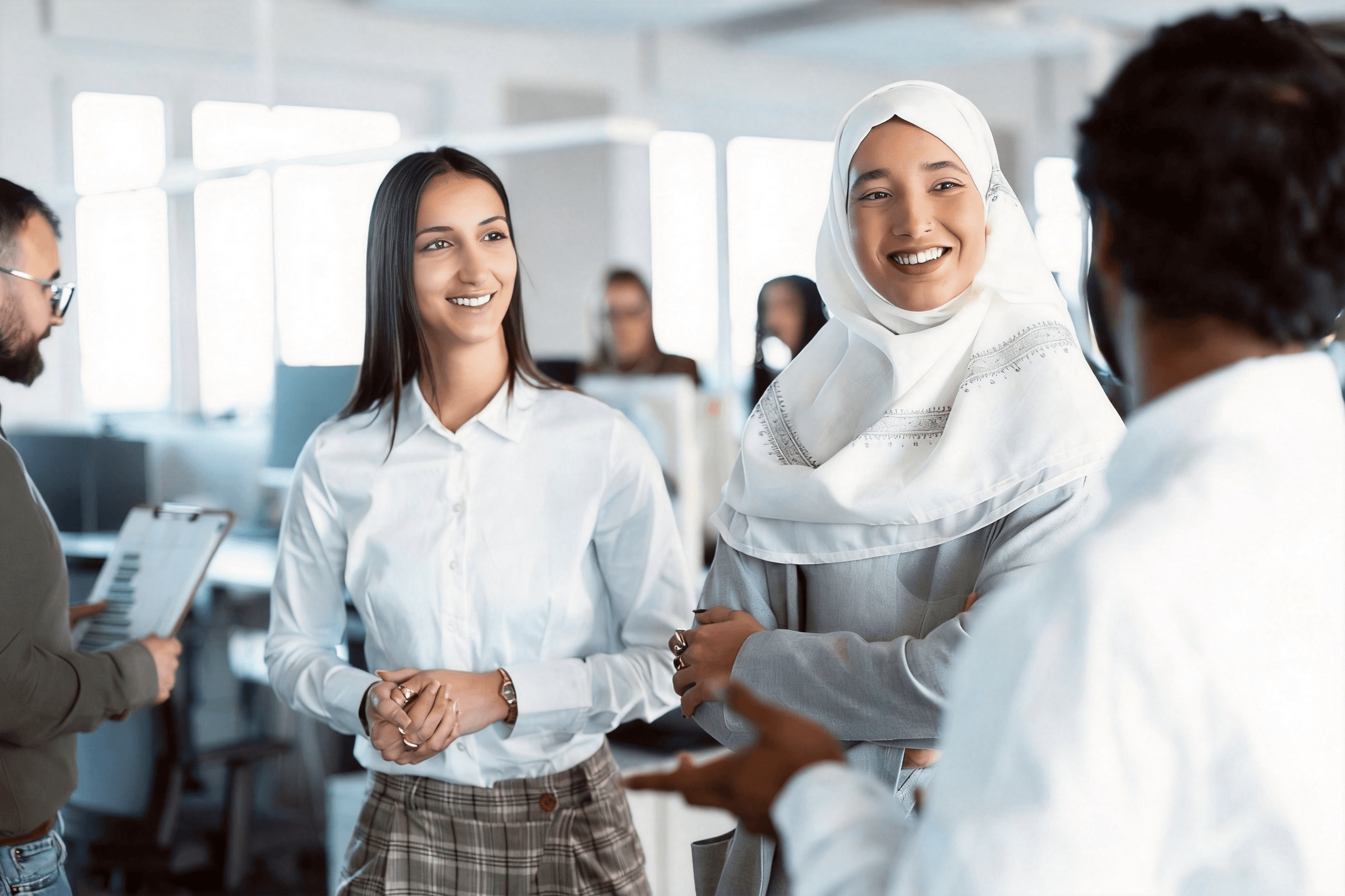 A diverse group of colleagues, including a woman wearing a hijab, talking together in an office